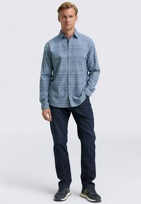 Camicia a righe blu con bottoni, realizzata in tessuto leggero, maniche lunghe e colletto, abbinata a jeans scuri e scarpe grigie.