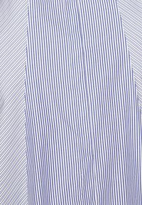 Tissu avec des rayures bleues et blanches alternant verticales et diagonales, montrant une couture où les motifs se rejoignent.