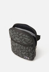 Borsa a spalla con motivo camouflage nero e grigio, dotata di chiusura con zip, caratterizzata da una texture morbida e un piccolo logo decorativo.