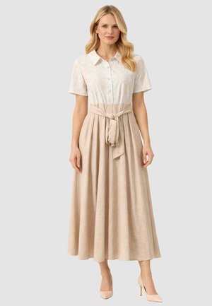 Donna che indossa un vestito beige con bottoni, maniche corte, top floreale con texture, vita annodata e gonna midi svasata, abbinato a tacchi beige.