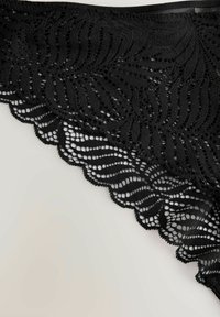 Black lace underwear featuring a wavy pattern, scalloped edges, and a textured design with open weave elements.