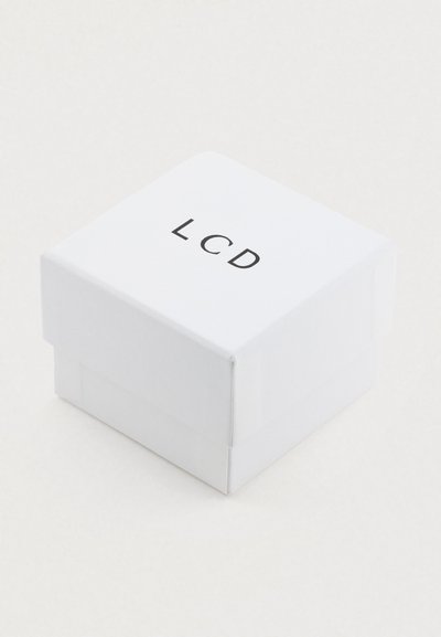 Maža balta dėžutė su juodai ant viršaus atspaustu užrašu „LCD“, padėta ant vienodo šviesios spalvos paviršiaus.