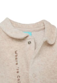 Prenda de forro polar de color rosa claro con cuello, que presenta una etiqueta azul y un botón de presión. "Donde hace frío" bordado en marrón.