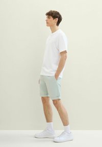 Biała bawełniana koszulka, jasnoszare szorty i białe trampki. Luźny krój z podwiniętym dołem szortów i teksturowanym materiałem. Prosty design.