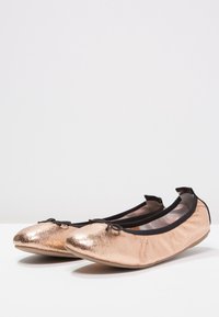 Bailarinas metálicas en color rosa dorado con textura suave, ribete negro y un detalle de lazo en la parte frontal. Punta redondeada y suela flexible para mayor comodidad.