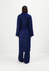Navy blue wool long coat with a collar, belted waist, and long sleeves, shown from the back with minimal accent detailing.
