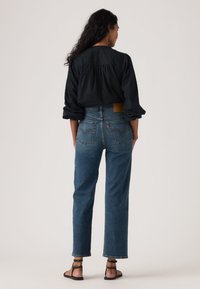 Τζιν παντελόνι από μπλε ντένιμ με ψηλή μέση και ίσια γραμμή, με πίσω τσέπες και δερμάτινο ταμπελάκι στη ζώνη της μέσης. Μαύρο μπλουζάκι και σανδάλια.