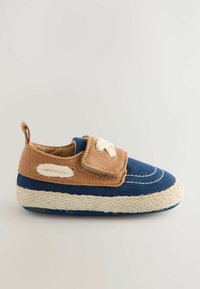 Chaussure en toile bleue avec une sangle en tissu marron, présentant un motif de couture blanche et une semelle en corde texturée. Style facile à enfiler.
