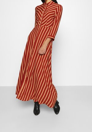 Kvinde iført en lang, rød og beige diagonalt striped knap-op kjole med trekvartærmer og sorte ankelstøvler.