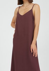 Burgundinsider-infons dress, jossa on syvä V-aukko ja ohuet hihnat. Valmistettu sileästä kankaasta, joka on rento ja ilman näkyviä kuvioita tai metalliosia.