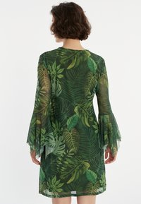 Grünes Kleid mit einem Blattmuster, aus durchscheinendem Stoff gefertigt. Es hat Glockenärmel und einen runden Ausschnitt, mit einer taillierten Silhouette.