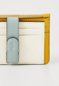 Portafoglio in pelle bianca strutturata con accenti gialli. Presenta una tracolla azzurro chiaro con logo e numerosi scomparti per carte per una migliore organizzazione.