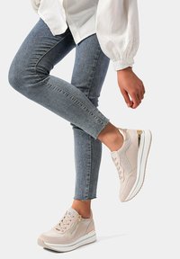 Sneaker beige con un mix di materiali lisci e scamosciati, dotate di una zip laterale, suola bianca e sottili dettagli metallici.