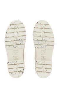 Suole di sneakers bianche con scanalature texture e macchie nere, con la scritta "CALVIN KLEIN JEANS" impressa al centro.