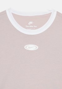 Világos rózsaszín rövidujjú póló fehér bordás kerek nyakkal. A mellkasán fehér Nike logó található, puha és sima anyagból készült.