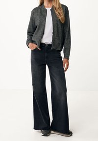 Veste bomber en tweed gris avec fermeture éclair, portée sur un t-shirt blanc ; associée à un jeans noir à jambes larges et des baskets grises.