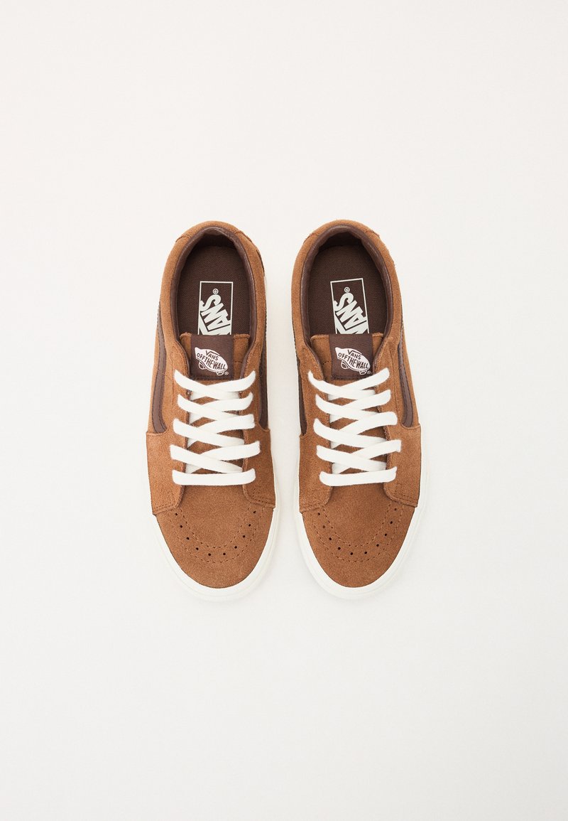 Baskets en suede marron avec des lacets blancs, design perforé à l'avant, et rayures latérales contrastantes en brun foncé. Logo "Vans" sur la languette. Semelle blanche.