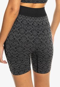 Schwarze Radshorts mit einem strukturierten Muster aus ineinandergreifenden Formen. Der Bund ist einfarbig schwarz und der Stoff hat ein weiches, dehnbares Finish.