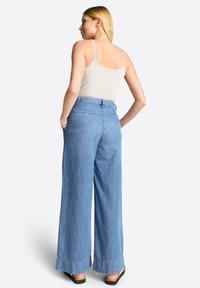 Svetlemodré džíny s širokými nohavicemi vyrobené z denimu s vysokým pasem. Zadní strana obsahuje minimální švy a kapsy. Stylizováno s lehkým topem bez rukávů.