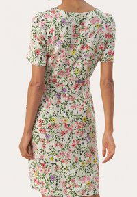 Robe fleurie à manches courtes, fabriquée en tissu léger. Fond blanc avec des fleurs colorées roses, violettes et jaunes ainsi que des feuilles vertes.