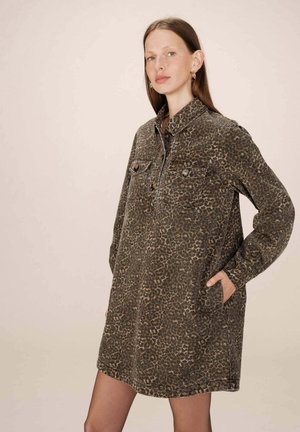 Robe chemise imprimée léopard en vert foncé et marron. Elle présente un col à boutons, deux poches poitrine et des manches longues avec des poignets.