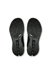 Suole di scarpe sportive nere con un motivo di grip testurizzato, frecce direzionali, bordi curvi e un pannello centrale liscio.
