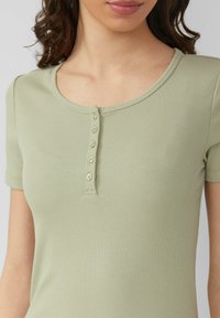 Jasnozielony prążkowany top z okrągłym dekoltem i krótkimi rękawami, z zapięciem na guziki składającym się z czterech jasnych guzików.