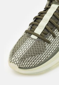 Chaussure de sport verte avec une tige en mesh texturé à motif losange, une semelle intermédiaire en plastique lisse et des lacets contrastants.