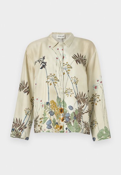 Blouse beige clair avec des motifs floraux verts, bleus et bruns, dotée de boutons sur le devant et d'un col classique. Manches longues. Texture en soie.