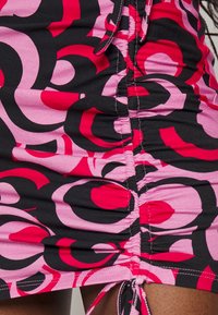 Gros plan d'une jupe froncée avec un motif abstrait en spirale rouge, rose et noir et un cordon noué à l'ourlet.