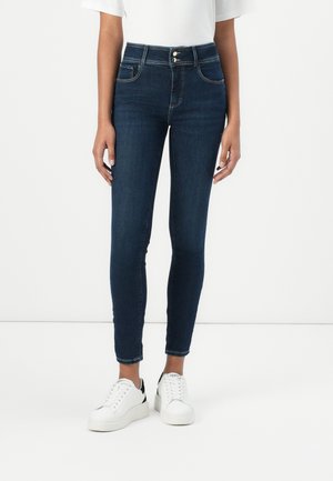 Dark denim skinny jeans with a high waist, front pockets, and button closures, paired with white platform sneakers. Classic fit and design.