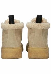 Bottines en suède beige clair avec un col en fourrure beige duveteux et des tirettes noires, présentant une semelle texturée marron clair.
