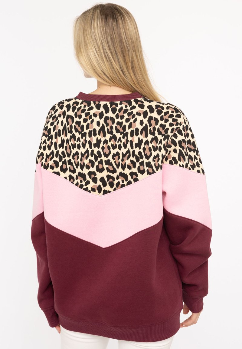 Bordeauxfarbener Hoodie mit Leopardenmuster im oberen Bereich, pinkem Zickzackdesign und geripptem Kragen. Weicher Stoff, lässige Passform.