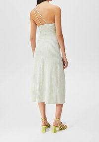 Grün-weiß kariertes Midikleid mit dünnen Trägern, tailliertem Oberteil und schwingendem Rock. Ein Paar grüne Sandalen mit Blockabsatz rundet den Look ab.