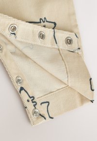 Kreemjas manustatud veluurkangas sinise loomamustriga. Nähtavad trukid ja õmmeldud ääred. Tekstuur on sooniline, pakkudes pehmet tunnet.