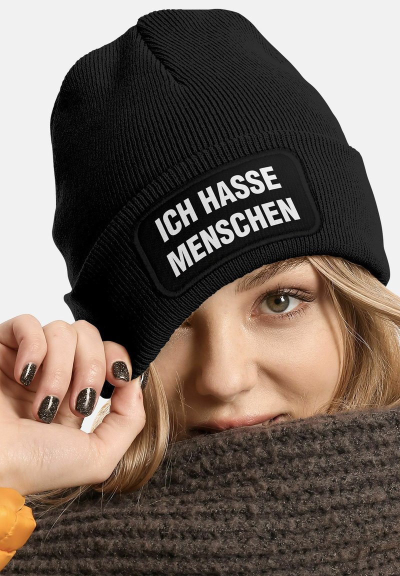 Black ribbed knit beanie featuring a rectangular, white text patch stating "ICH HASSE MENSCHEN." Soft texture, fitted design.