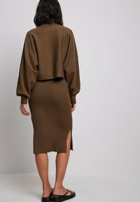 Brun stickad kort tröja med ballongsärmar, kombinerad med en brun ribbad midikjol med en sidoklyfta och platta svarta sandaler.