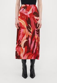 Plisserte maxi-skjørt i røde og rosa nyanser med blomsterdesign. Elastisk midjebånd, lett stoff, paret med svarte spisse støvler.