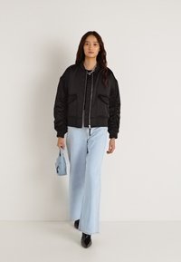 Μαύρο μπουφάν bomber με φερμουάρ, δύο εμπρόσθιες τσέπες, συνδυασμένο με ανοιχτό μπλε φαρδιά τζιν παντελόνια και μια μικρή ανοιχτό μπλε τσάντα.