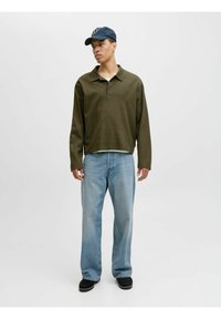 Polo vert à manches longues avec un col, jeans clairs et chaussures noires. Le polo a un tissu texturé et une coupe décontractée, avec des coutures visibles.
