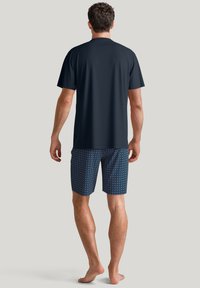 Marineblauw T-shirt met korte mouwen, gecombineerd met gestreepte blauwe shorts met een geometrisch patroon, weergegeven vanaf de achterkant tegen een neutrale achtergrond.