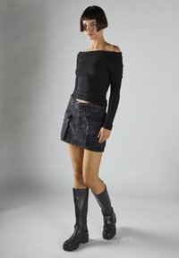Top nero lungo a maniche lunghe scollato sulle spalle, con trama a coste, abbinato a una minigonna in denim nero con tasche e cintura. Stivali neri al ginocchio.