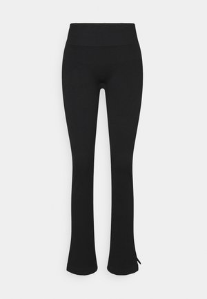 Leggings noirs taille haute avec une coupe slim et un léger évasement aux chevilles, avec une petite fente latérale sur chaque jambe.