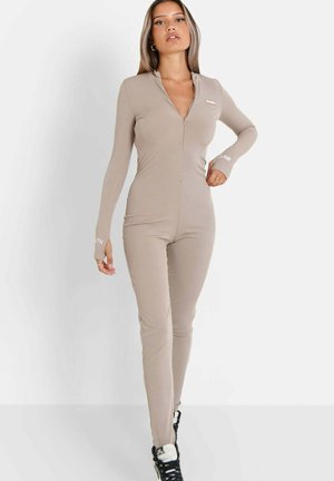 Tutina beige a coste con maniche lunghe e zip frontale. Presenta un design attillato e fori per il pollice nei polsini. Accentuata con brand bianco.