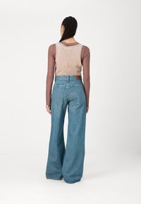 Jeans din denim, cu picioare largi, de culoare bleumarin deschis, cu talie înaltă, asortați cu un top fără mâneci de culoare bej. Include un eticheta pe spate și detalii subtile de cusătură.