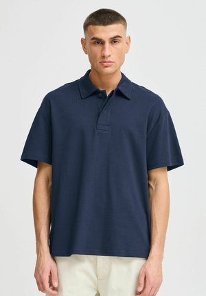 Navy blue polo shirt made of smooth fabric, featuring a buttoned collar, short sleeves, and a relaxed fit. No patterns or additional accents.