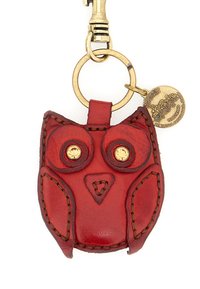 Portachiavi a forma di gufo in pelle rossa con hardware dorato, caratterizzato da accenti cuciti e occhi simili a gemme. Include un'etichetta da brand rotonda.