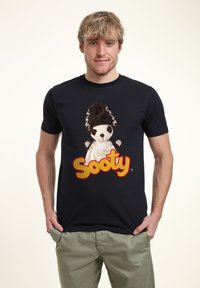 Černé bavlněné tričko s potiskem loutky s hnědými vlasy a bílým oblečením, doplněné textem "Sooty" v tučných červených písmenech.
