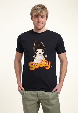 Černé bavlněné tričko s potiskem loutky s hnědými vlasy a bílým oblečením, doplněné textem "Sooty" v tučných červených písmenech.