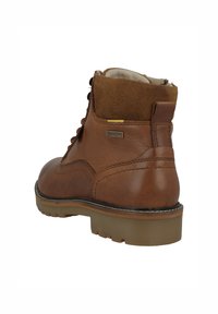 Botines de cuero marrón con una superficie lisa, collar de ante y suela de goma. Presentan herrajes amarillos y detalles de costura en contraste.